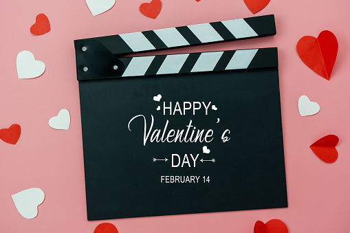 Table top view aerial image of decoration valentine's day background concept.Flat lay essential items colorful love shape paper cut with welcome word on movie clapper with modern pink wallpaper.