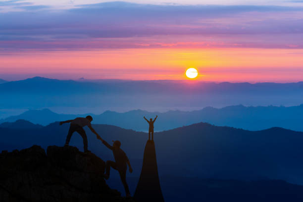 팀워크 우정 하이킹은 산, 일출에서 서로 신뢰 지원 실루엣을 도와줍니다. 등산 팀 아름다운 일출 풍경의 상단에 서로 를 돕는 두 남자 등산객의 팀워크 - men on top of climbing mountain 뉴스 사진 이미지
