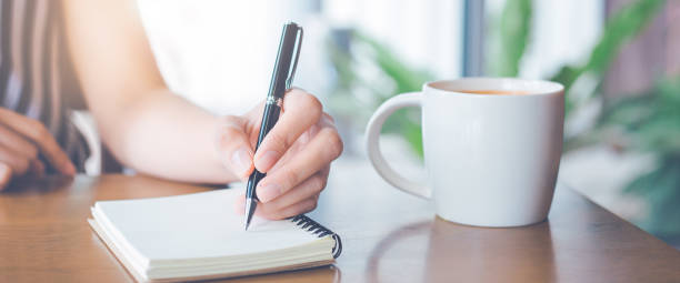 istock Woman hand is writing on notepad with a pen in the office.Web banner. 1202865698