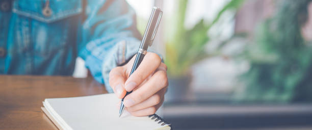 istock Woman hand is writing on notepad with a pen in the office. 1202865702
