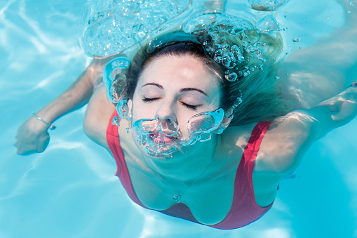 Beautiful woman with her eyes closed emerging from swimming underwater and shooting air bubbles. Leisure concept.