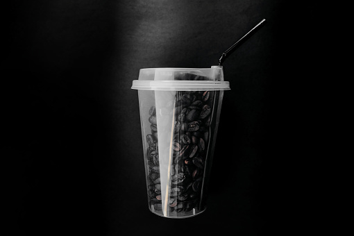 stylish transparent tall glass with a black straw filled with raw coffee grains on a flat dense background in the style of minimal total black, stylish coffee advertisement
