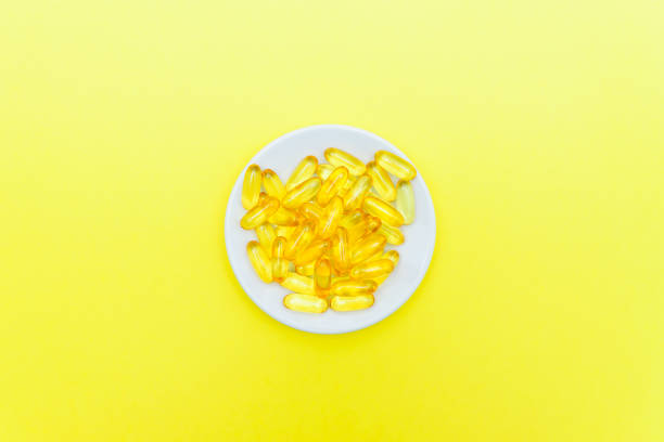 istock Fish oil capsules in a white plate on yellow background. Top view, flat lay, copy space. 1202888964