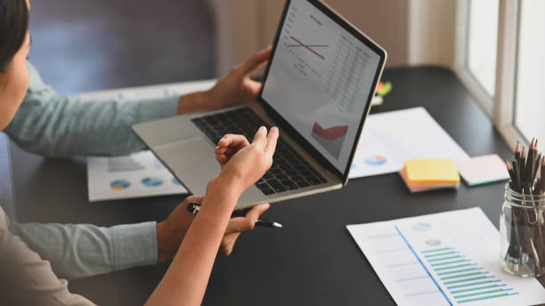 istock Cropped shot of young business development team are discussing about them projects by using laptop with graphic chart and sitting at the modern meeting table. 1202890053