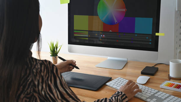 istock Behind view of young creative designer sitting at wooden working desk using graphic tablet for selecting color from color management/color palette program. Graphic design concept 1202890079