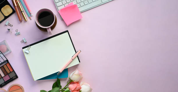 istock Top view image of feminine working desk including coffee cup, modern keyboard, notebook, pencil, bouquet and cosmetics putting on it. Women's working desk concept. 1202890306