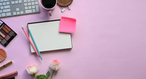 istock Top view image of feminine working desk including coffee cup, modern keyboard, notebook, pencil, bouquet and cosmetics putting on it. Women's working desk concept. 1202890307