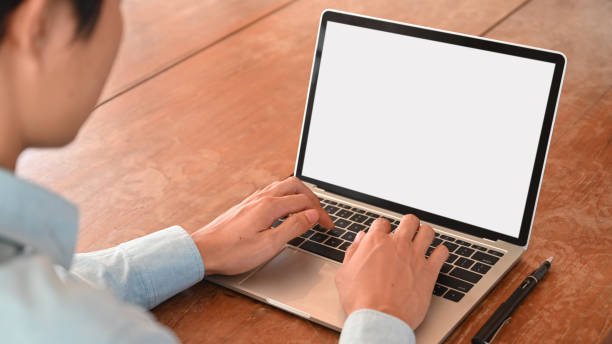 istock Behind shot through shoulder of smart man working as insurance statistic while typing on white blank screen laptop with wooden working desk as background. 1202890548