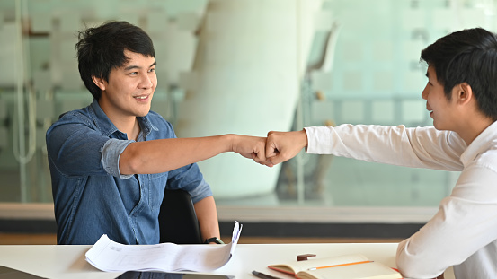 Fist-bump or knuckle-bump of businessmen after finished discussing about project problem with the modern meeting room as background.