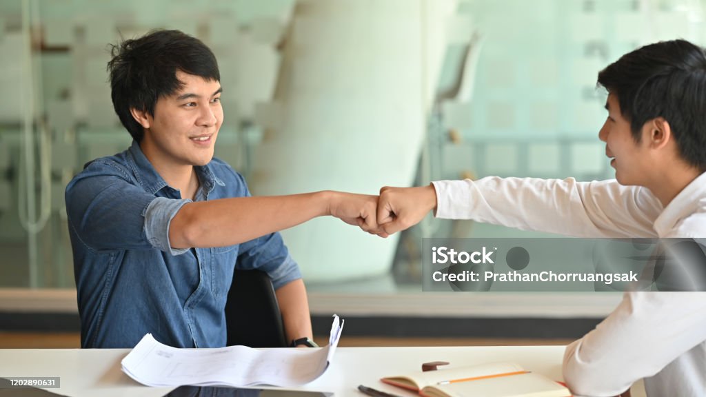 Fist-bump or knuckle-bump of businessmen after finished discussing about project problem with the modern meeting room as background. Fist Bump Stock Photo
