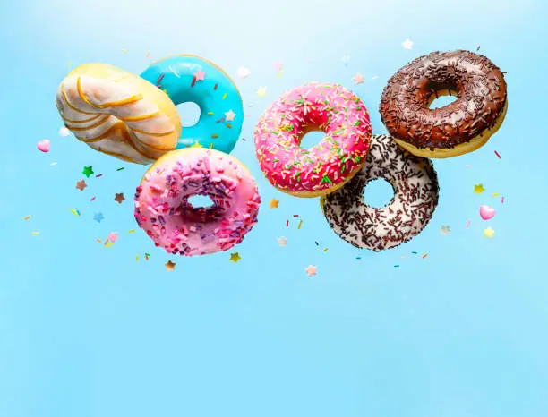 Mix of delicious multicolored doughnuts with various sprinkel flying on blue background. Copy space