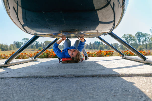 Smiling young woman lying on a cart under the helicopter and doing maintenance work