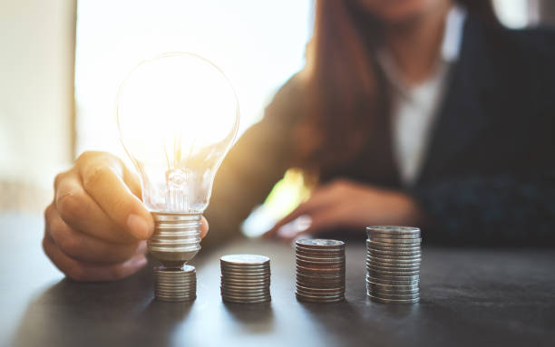 istock Businesswoman holding and putting lightbulb on coins stack on table 1202896799
