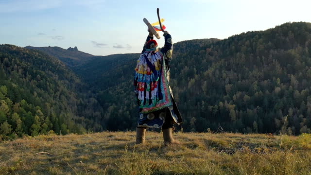 Siberian shaman performs a ritual dance and beats a tambourine on the top of the mountain.