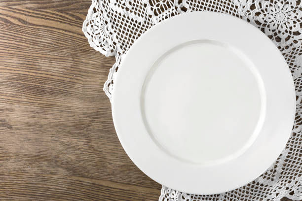 istock Empty white plate served on old style wooden table with handmade tablecloth. Top view 1202900599
