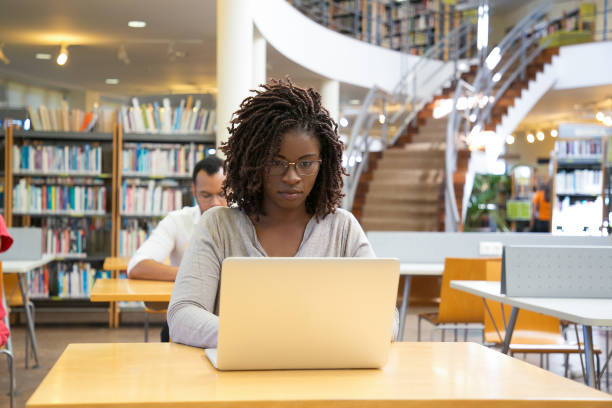 istock Front view of thoughtful woman working with laptop at library 1202905029