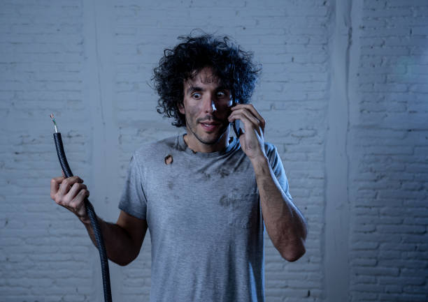 Portrait of young man holding electrical cable after domestic accident with dirty burnt funny face expression calling desperate with mobile phone asking for help. Electricity repairs and DIY concept. retrato de joven sosteniendo cable eléctrico después de un accidente doméstico con la expresión de la cara divertida quemada sucia llamando desesperado con el teléfono móvil pidiendo ayuda. reparaciones de electricidad y concepto de bricolaje.