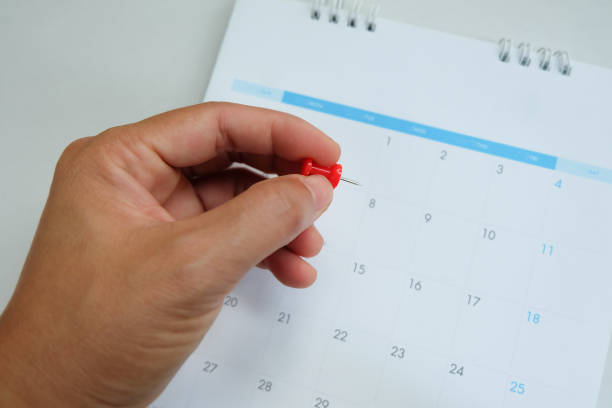 Close up red pin in hand on calendar.