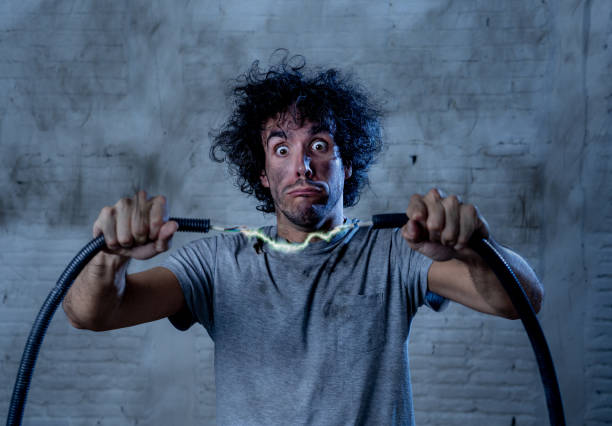 istock Man getting electric shock connecting broken electrical cables at home. Husband having domestic accident being electrocuted with dirty burnt face and crazy expression. Electricity DIY repairs danger. 1202907382