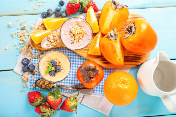 istock Orange persimmon blueberry smoothie with granola  and fruits. Selective focus. Copy space. Top view 1202911342
