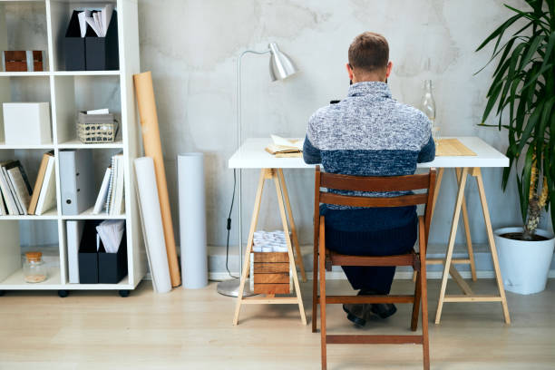 istock Back view of an Attractive freelance male sitting in modern office and typing on notebook. 1202911421