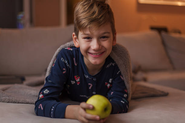 istock Happy little boy with an apple on sofa at home. 1202911730