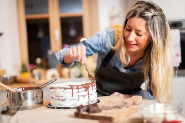 Woman baking at home: Decorating chocolate sponge cake