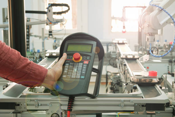 istock Close up of man's hand holding teach panel to control robot arm which is integrated on smart factory production line. industry 4.0 automation line equipped with sensors and robot at background. 1202914027