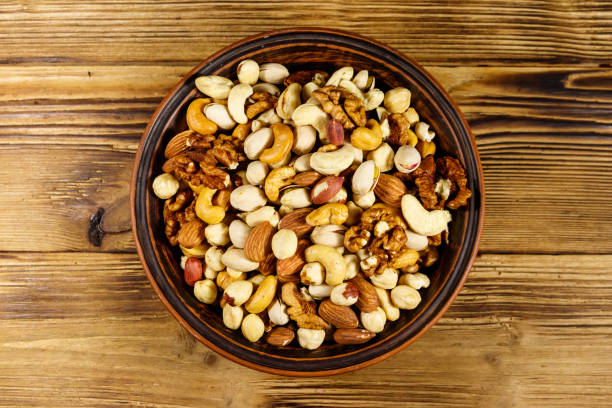 istock Mixed nuts on wooden table. Walnuts, pistachio, almond, peanut, cashew, hazelnut in ceramic bowl. Healthy eating concept. Top view 1202914966