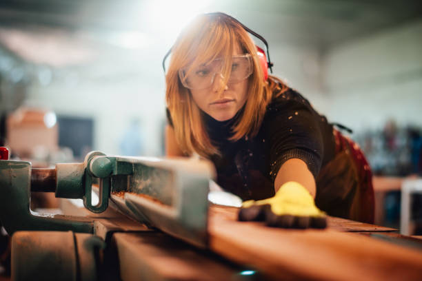 istock Female carpenter pushing a plank to cut it using a saw guide 1202916152
