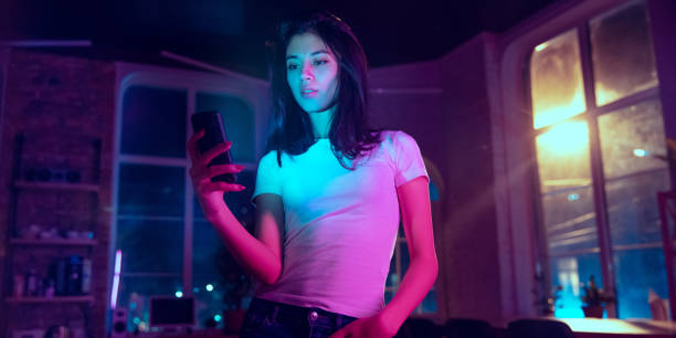 Cinematic portrait of handsome young woman in neon lighted interior Serfing. Cinematic portrait of handsome stylish woman in neon lighted interior. Toned like cinema effects in purple-blue. Caucasian female model using smartphone in colorful lights indoors. Flyer. cinematic music photos stock pictures, royalty-free photos & images