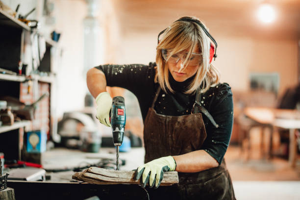 una mujer carpintera cambiando el papel de una lijadora orbital mientras trabajaba en una tienda - taladro fotografías e imágenes de stock