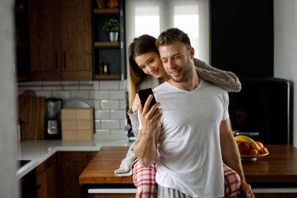 istock Young affectionate couple looking at mobile phone in the kitchen 1202920791