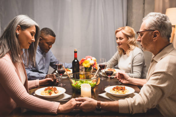 istock multicultural friends holding hands and praying during dinner 1202921587