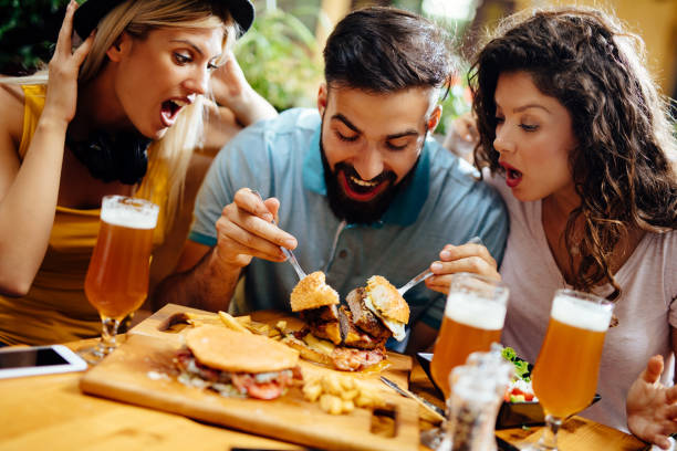 istock Young man eating oversized burger in a fast food restaurant 1202921679