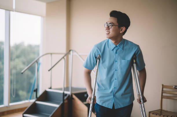 un paziente maschio cinese asiatico che si riprende dalla ferita alla gamba e cammina con le stampelle in ospedale - thinking young men indoors part of foto e immagini stock
