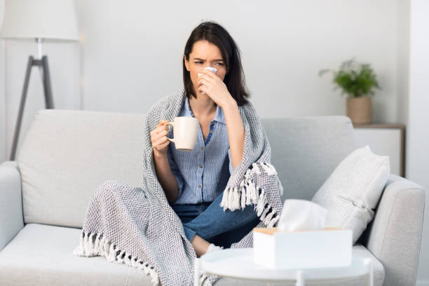 istock Sick girl wrapped in blanket drinking hot tea 1202925034