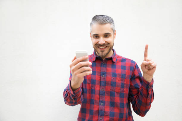 istock Cheerful man holding smartphone and pointing up with finger 1202927915
