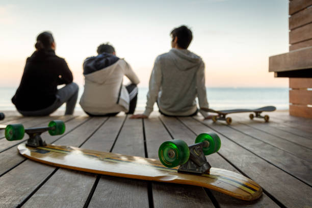 istock A skateboard with three young boys in the background watching the sunset on the beach 1202940712