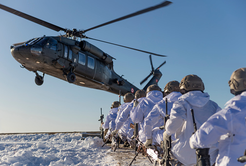 Şırnak, Turkey - January 27, 2020: Turkish Army Special Forces soldiers kneeling down in a row and waiting for boarding on a landing Sikorsky UH-60 Black Hawk military helicopter during an operation against PKK terrorist organization in winter. (ATTENTION FOR INSPECTOR: This photo was produced at a public location where photographic rights are not protected. It is not a military base. There s no need for property release.)