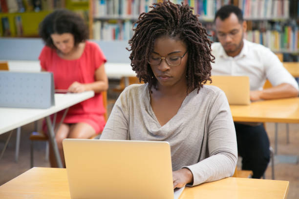 istock Front view of concentrated woman working with laptop at library 1202947765