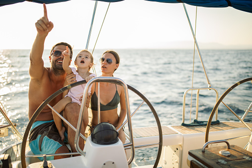 Beautiful happy family enjoying together their vacation on sailboat. They are steering on yacht