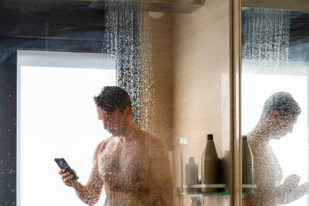 携帯電話を使用しながらシャワー水の下の男 - men naked shower bathroom ストックフォトと画像