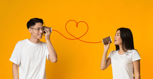 istock Young asian couple with can phone on orange background 1202952122