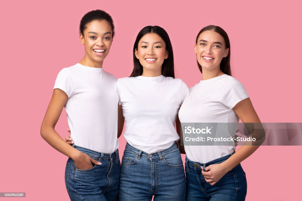 Three Pretty Girls Embracing Smiling To Camera Posing In Studio Three Pretty Girls Embracing Smiling To Camera Posing In Studio Over Pink Background. Female Friendship Concept T-Shirt Stock Photo