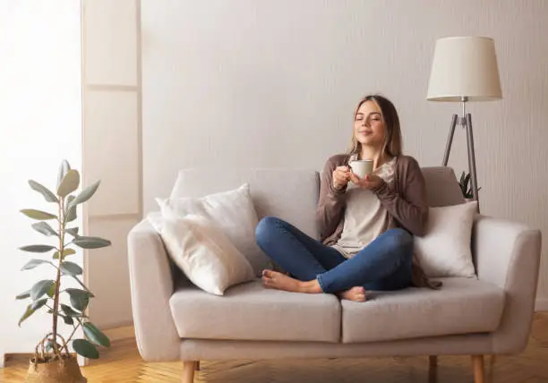 Photo of Young coffee lover sniffing hot drink at cozy home interior