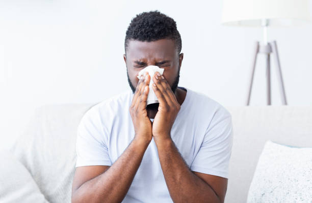 istock Sick african guy cleaning his snotty nose at home 1202952876