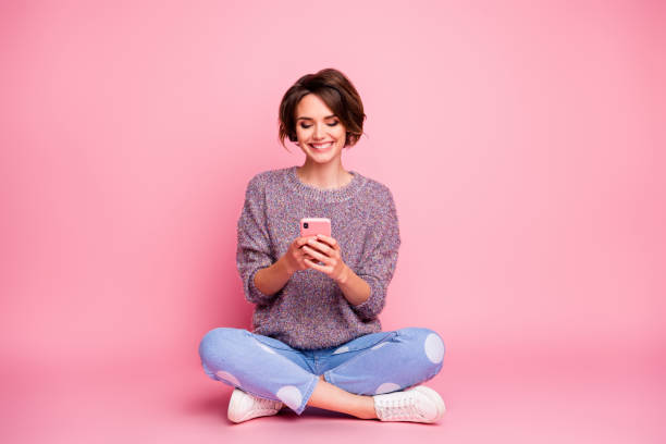 retrato de su ella atractiva encantadora encantadora encantadora agradable alegre alegre alegre chica de pelo marrón sentado usando celda 5g aplicación aislada sobre el fondo de color pastel rosa - con las piernas cruzadas fotografías e imágenes de stock