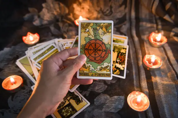 Photo of Hand holding tarot card with candlelight on the darkness background for Astrology Occult Magic illustration - Magic Spiritual Horoscopes and Palm reading fortune teller concept