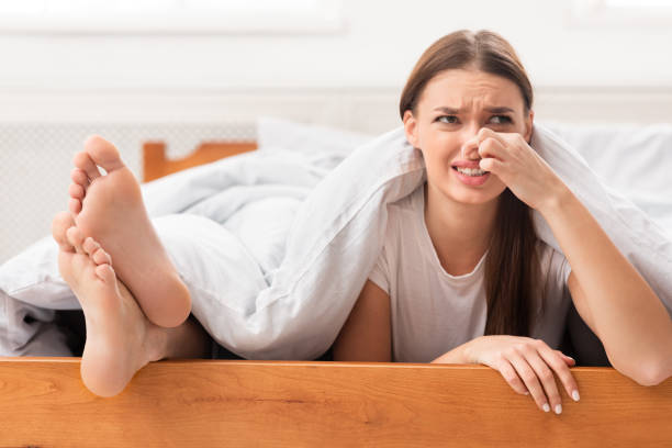 Woman Lying Near Boyfriend's Feet Pinching Nose In Bed Indoor Smelly Legs. Disgusted Woman Lying Near Her Boyfriend's Stinky Feet And Pinching Nose In Bed Indoor. Selective Focus unpleasant smell stock pictures, royalty-free photos & images